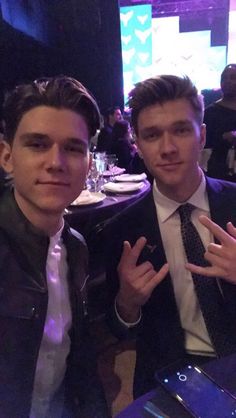 two men posing for the camera at a dinner table with their hands in the air