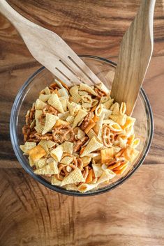 a glass bowl filled with pasta and nuts next to a wooden spoon on top of a table