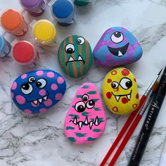 painted rocks with faces on them next to paintbrushes and watercolors in the background