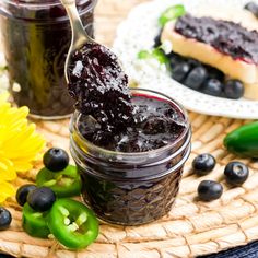 blueberry jam in a glass jar with spoon next to it on a wicker tray