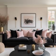 a living room with black couches and pink pillows