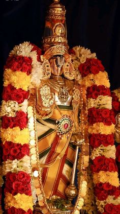 the statue is surrounded by red and yellow flowers in front of a black backdrop with gold trim