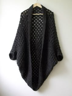 a black crocheted cardigan hanging on a white wall