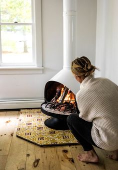 a woman kneeling down in front of an open fire place that is on top of a rug