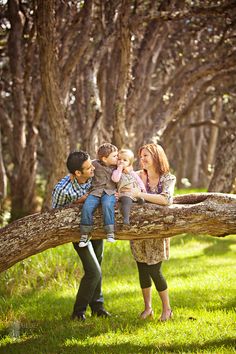 three adults and two children are playing on a tree branch in the grass with trees behind them