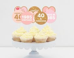 cupcakes with pink and gold frosting sitting on a cake plate in front of white backdrop