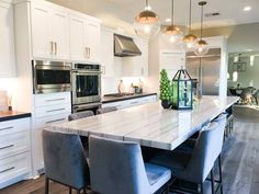 a large kitchen with white cabinets and marble counter tops, stainless steel appliances and an island in the middle