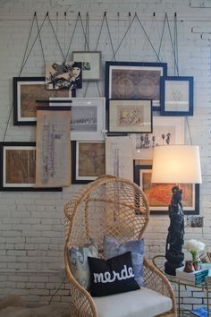 a wicker chair sitting in front of a white brick wall with pictures on it