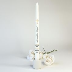 a white candle and some flowers on a white tablecloth with a cross in the middle