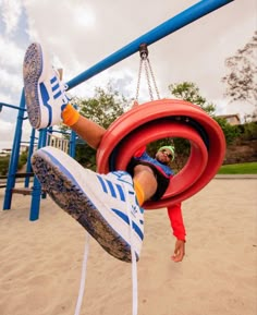 a man is hanging upside down on a tire in a playground with his feet up