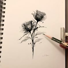 a person holding a pencil in their left hand and drawing flowers on paper with black ink