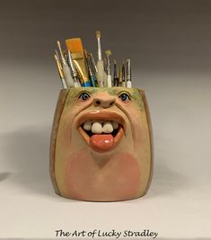 the toothbrush holder has many different brushes in it's mouth and is shaped like a face