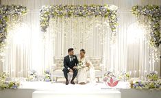 a bride and groom sitting on a stage at their wedding ceremony in front of floral decorations