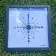 a shadow box with some glass beads in it on the grass and one is holding a cell phone