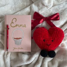 a crocheted red heart next to a book and pen on a white blanket