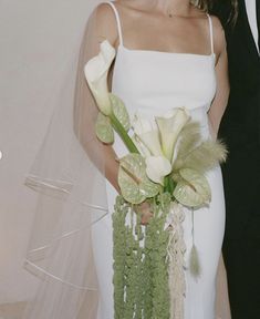 a bride and groom standing next to each other in front of a white wall with flowers on it