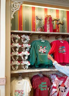 a woman is looking at t - shirts on display in a clothing store with mickey mouse ears