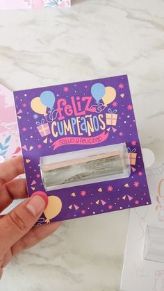 a person holding up a purple card with the word feliz cumpanos on it