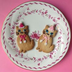 two decorated cookies sitting on top of a white plate with pink and gold trimmings