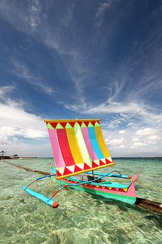 a colorful sail boat floating on top of the ocean