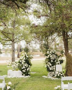 an outdoor ceremony setup with white flowers and greenery on the ground, surrounded by trees