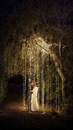 a bride and groom standing under a tree covered in lights