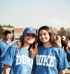 two young women standing next to each other in front of a group of people wearing blue shirts