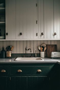 a kitchen with white cupboards and black counter tops is pictured in this image, there are utensils on the sink