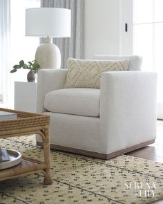 a living room with a white chair and lamp on the side table in front of a window