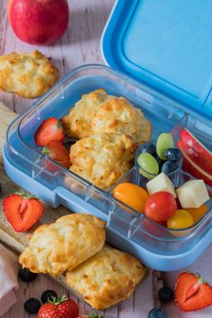 a plastic container filled with fruit and muffins next to other food on a table