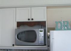 a microwave oven sitting inside of a kitchen next to white cupboards and counter tops