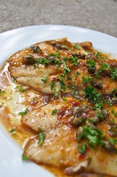 a white plate topped with fish covered in sauce and garnished with parsley