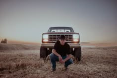 a man squatting in front of a truck on a dry grass field at sunset