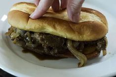 a hand reaching for a sandwich on a plate with onions and meat in the middle