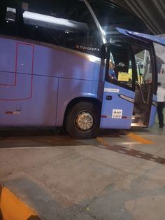 a blue bus parked in a parking lot next to a man standing on the sidewalk