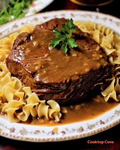 a white plate topped with meat and pasta covered in gravy on top of a wooden table