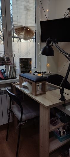 a desk with a lamp, computer monitor and books on it in front of a window