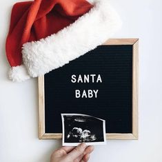 a santa hat on top of a black and white sign with the words santa baby