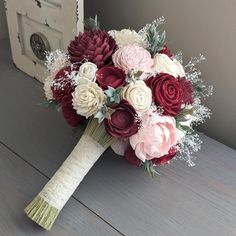 a bridal bouquet with red, white and pink flowers on a wooden table next to a mirror