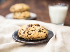 two chocolate chip cookies on a black plate with a glass of milk in the background