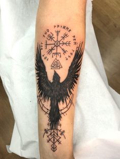 a black bird with an arrow and compass tattoo on the arm