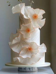 a white and orange cake with flowers on it sitting on a table next to a wall