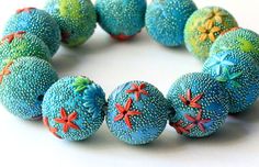 a bracelet made out of blue and green balls with red stars on them, sitting on a white surface