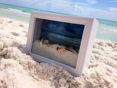 an empty photo frame sitting in the sand at the beach