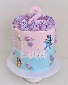 a pink and blue two tiered cake with flowers on the top is decorated with cartoon characters