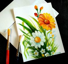 two cards with flowers painted on them next to paintbrushes and watercolor pencils