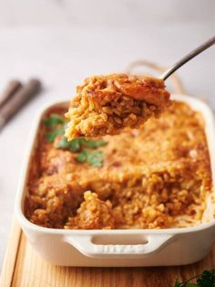 a spoon full of food is being lifted from a casserole dish with parsley