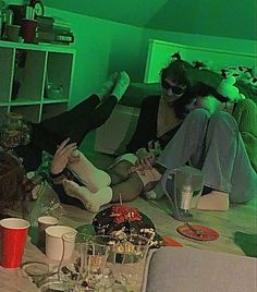 two women are sitting on the floor in a room with green lights and wine glasses