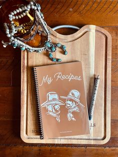 a wooden tray topped with a notebook next to a pen and glass jar on top of it