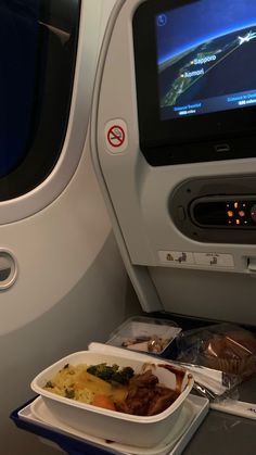 an airplane tray with food on it next to the seat belt and television screen in the back